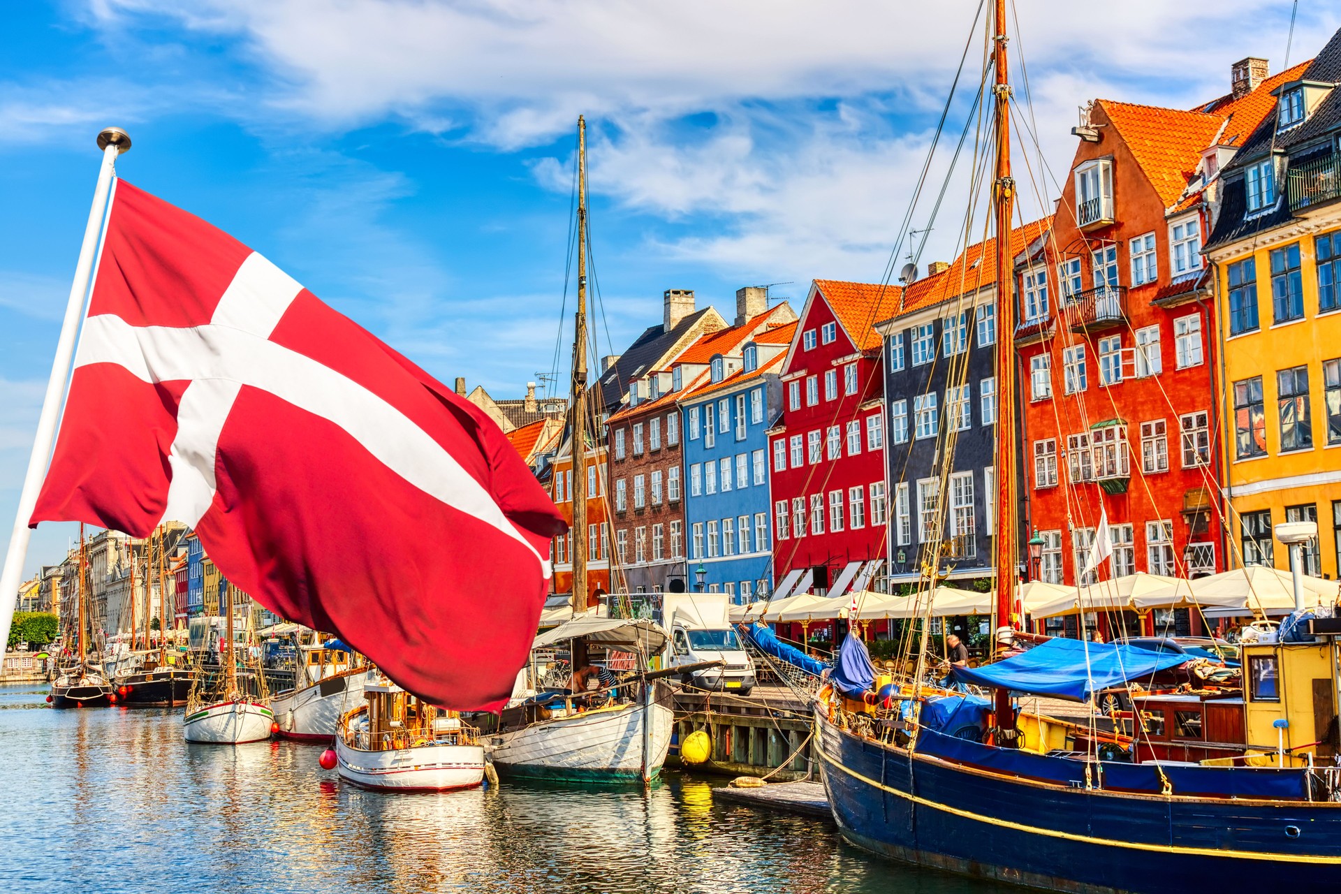 Copenhagen iconic view. Famous old Nyhavn port in the center of Copenhagen, Denmark during summer sunny day with Denmark flag on the foreground.